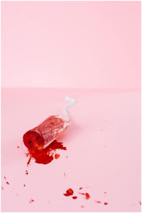 Close-up of a blood-stained tampon on a pink surfa