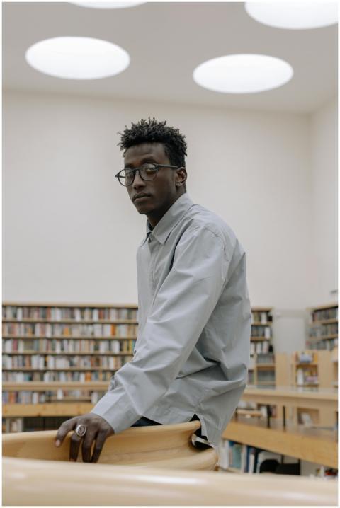 A thoughtful man in a library setting wearing eyeg