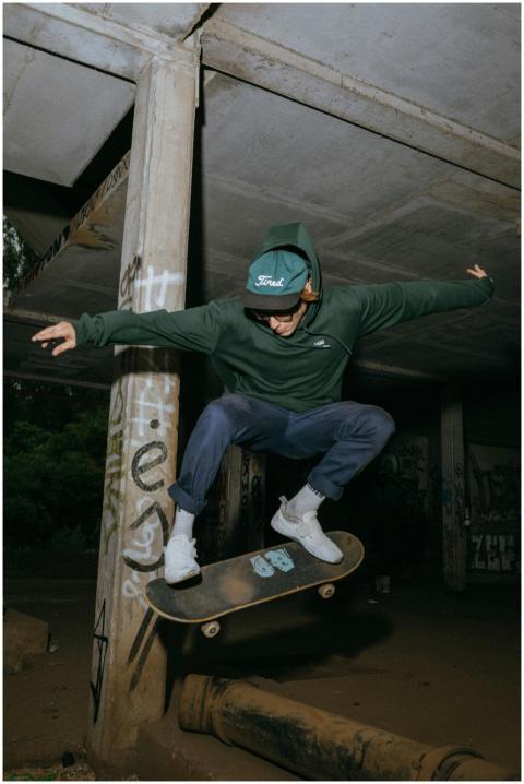 A young man in a green hoodie performs skateboardi
