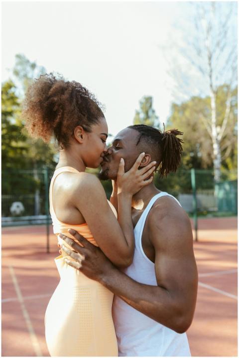 Loving couple sharing a kiss on a sunny tennis cou