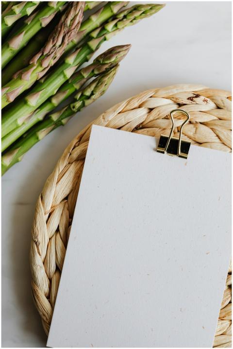 Fresh asparagus stalks next to blank paper on a wi
