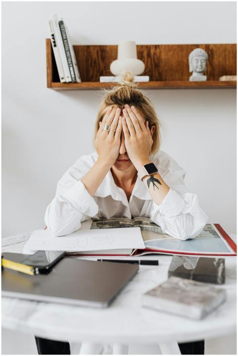 A woman sits at a home office desk overwhelmed, wi