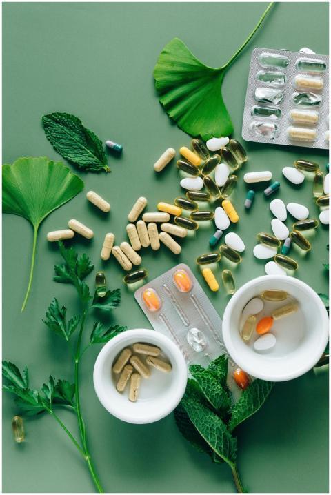 Flat lay of assorted pills and herbs on green surf