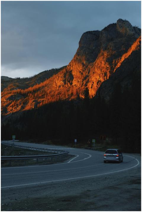 A car on a winding road with mountains illuminated