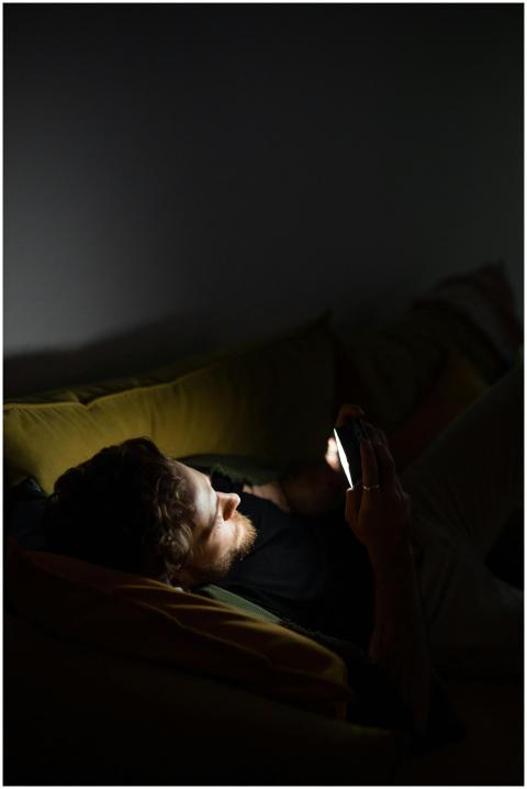 A man lounging on a couch playing games on his sma
