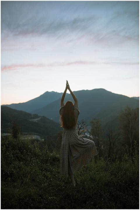 A woman in a dress performs tree pose against a mo