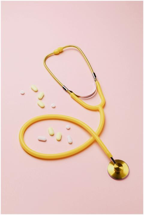 A yellow stethoscope and assorted pills on a pink