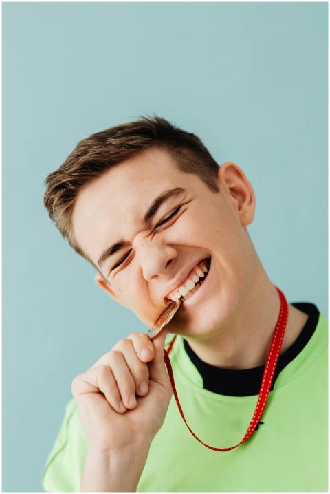 Joyful teen biting a gold medal on a light backgro