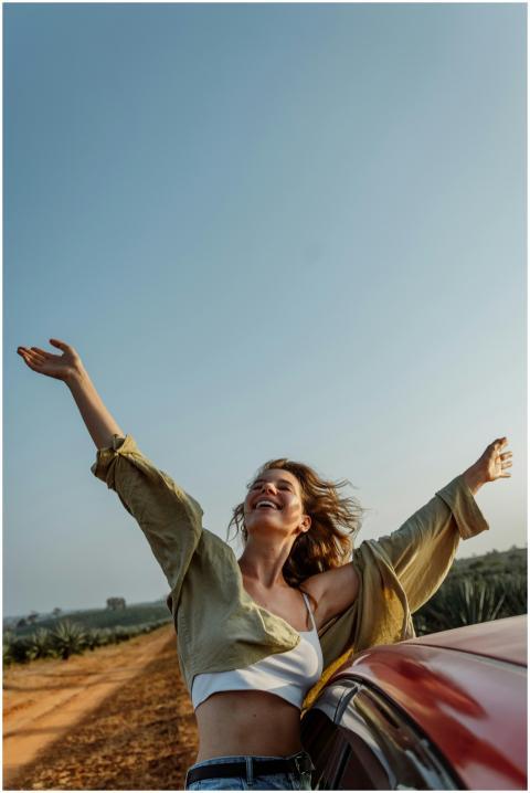 Woman joyfully stretches arms beside car on a sunn