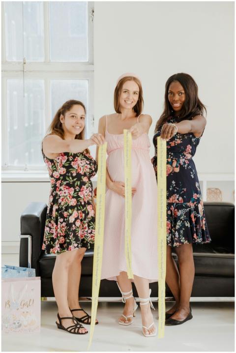 Three smiling women at a baby shower, holding tape