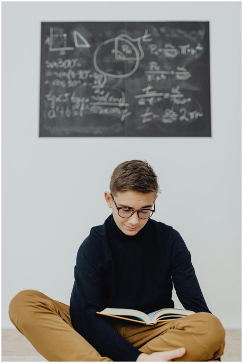 Teenage boy reading in front of chalkboard with ma