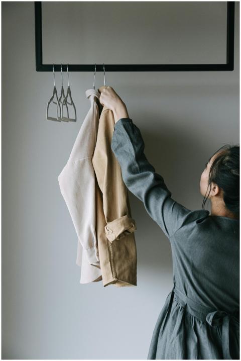 A woman arranges coats on a clothes rack indoors.