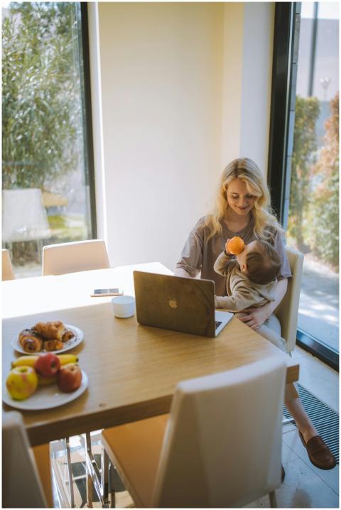A blonde mother multitasks with her baby and lapto