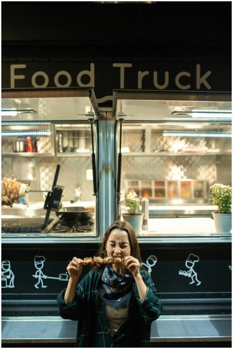 A woman savoring a kebab outside a trendy food tru
