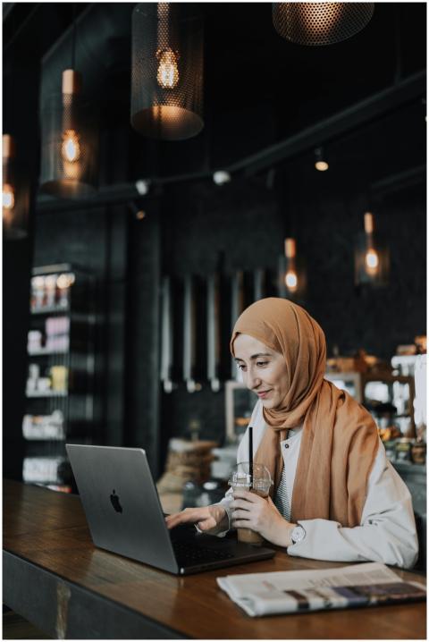 Woman in headscarf working on laptop and drinking