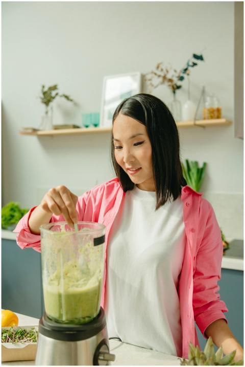 Asian woman making a healthy green smoothie in a m