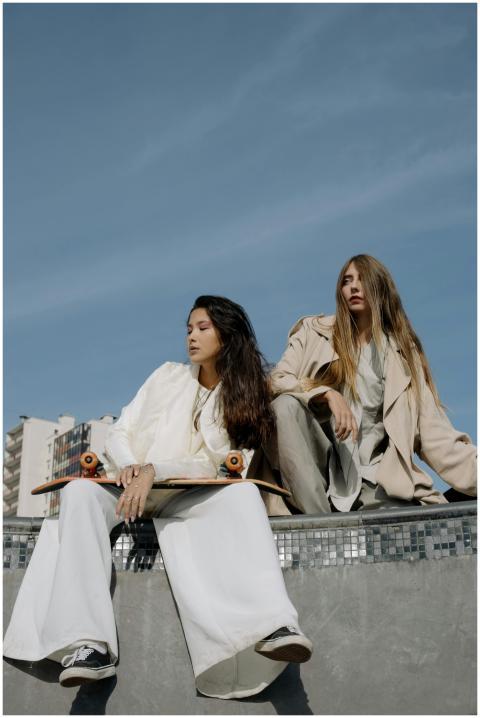 Two young women in stylish outfits sit with skateb
