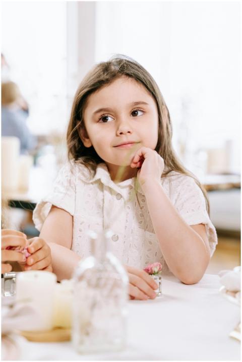 A young girl in a white dress sits thoughtfully at