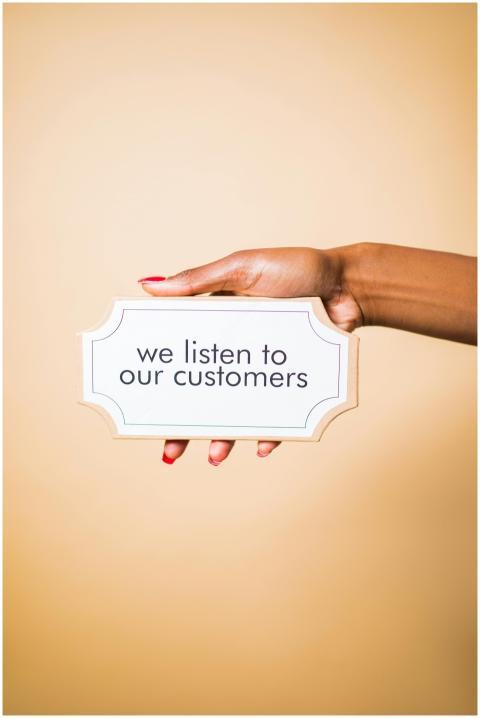 A hand holding a sign saying 'we listen to our cus