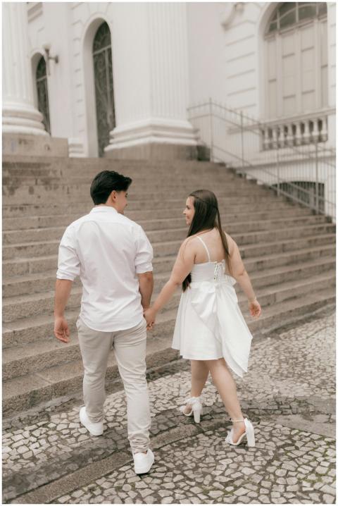 A couple in white attire walking hand in hand on h