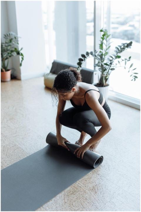 Woman rolling up yoga mat in sunlit studio, surrou