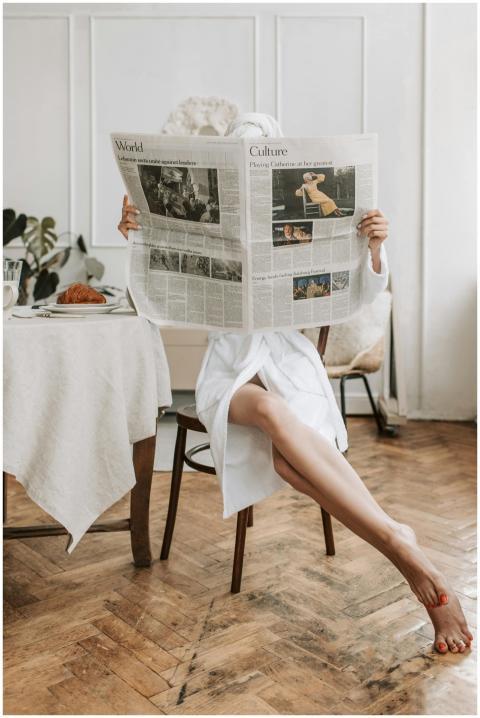 Woman in bathrobe reading newspaper barefooted, en