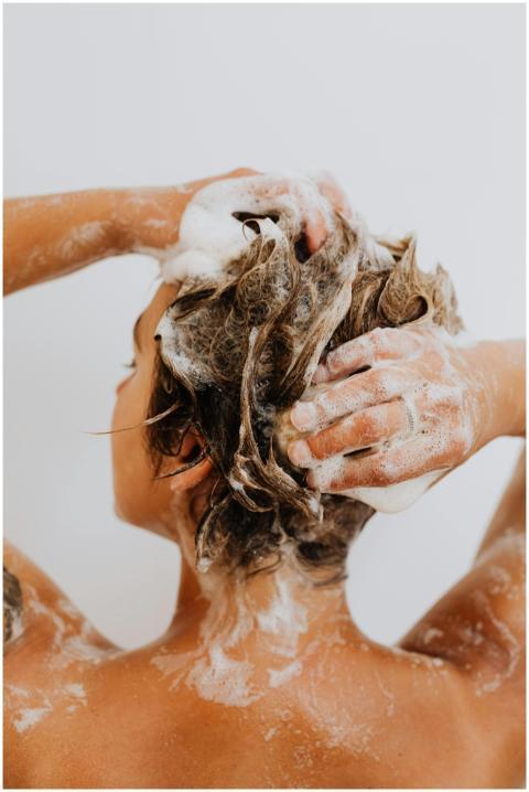 Back view of a woman washing her hair in a shower