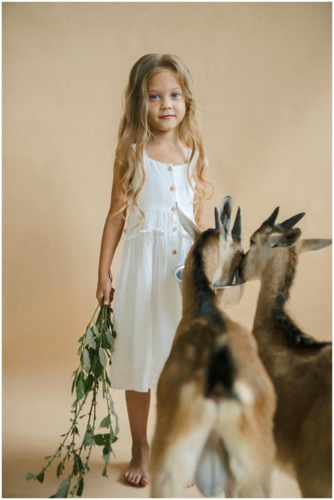 A young girl in a white dress holds leaves and sta