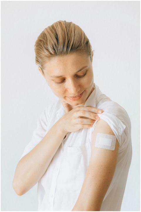 A smiling woman displays a bandage on her arm afte