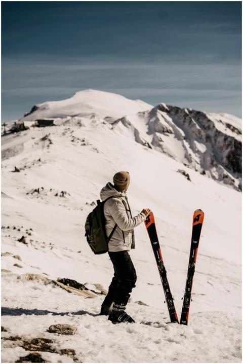 A skier stands with skis, looking at a snow-covere
