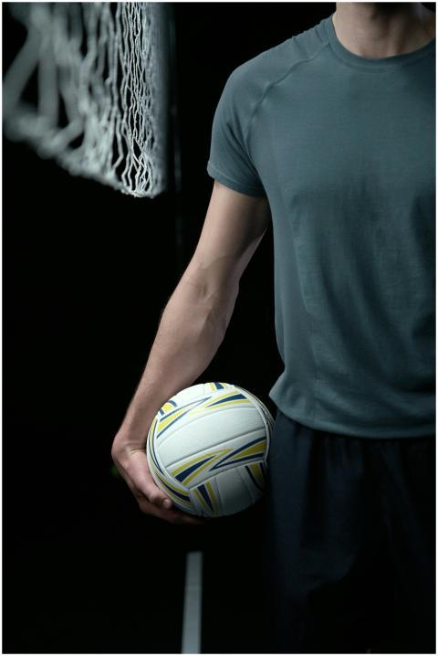 A male athlete holding a volleyball next to a net,