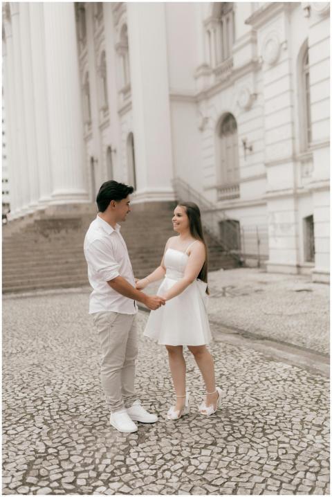 A couple in white outfits holding hands, standing