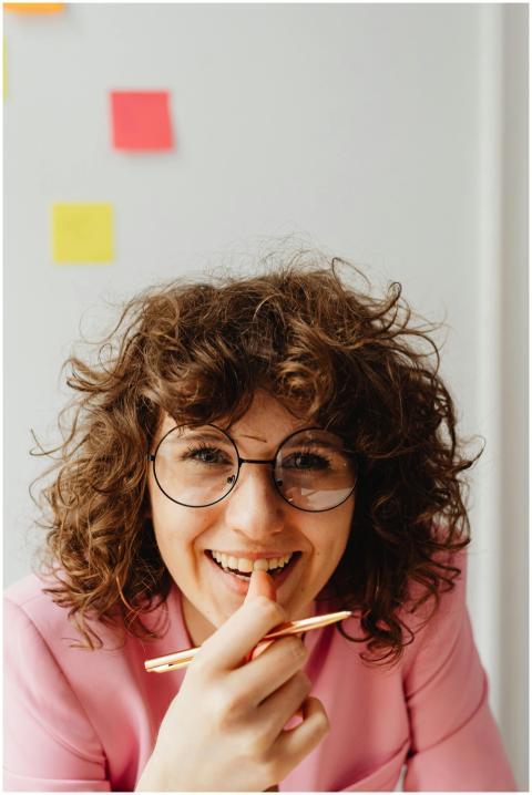 Curly-haired woman in glasses, wearing pink, smili