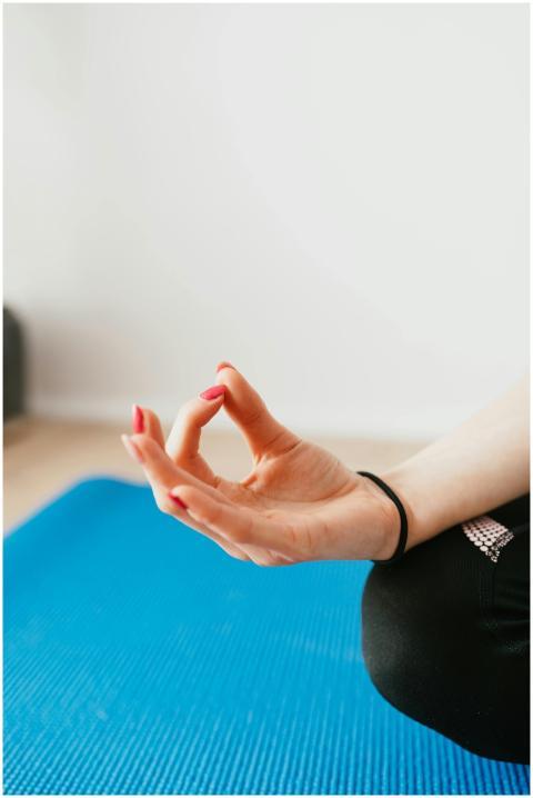A woman's hand in a yoga mudra pose on a blue mat,