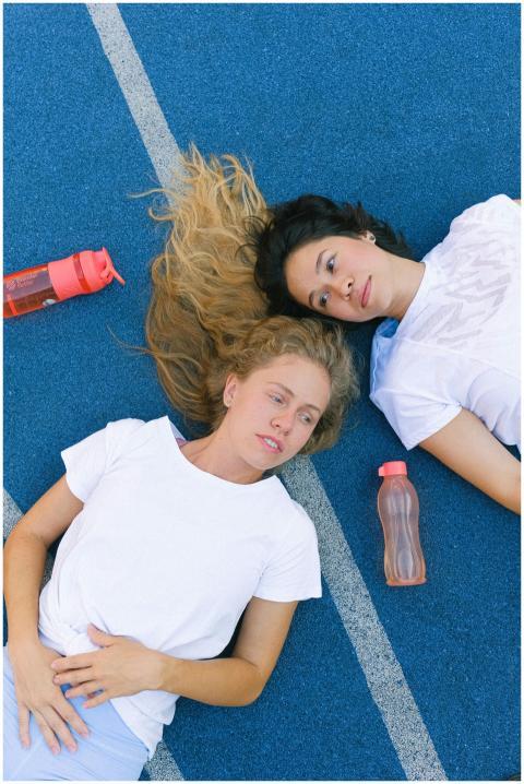 Two women in activewear resting on a track with wa