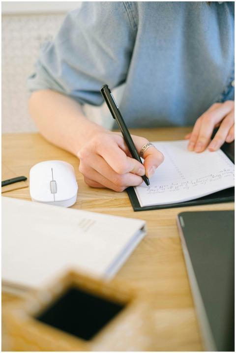 Close-up of a woman writing notes at a desk with a