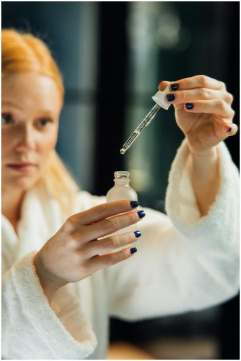 Blonde woman in a bathrobe applying serum with a d