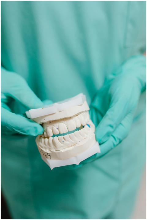 A dentist wearing gloves holds a dental model, ill