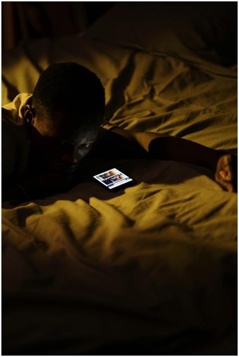 A man lying in bed at night, engaged with his smar
