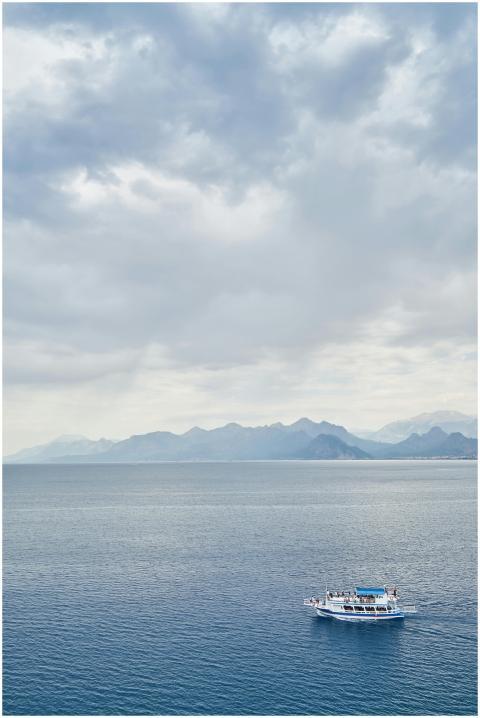 A lone boat sails across a tranquil sea beneath cl