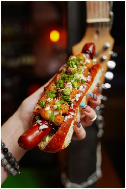 Close-up of a gourmet hot dog with toppings, held