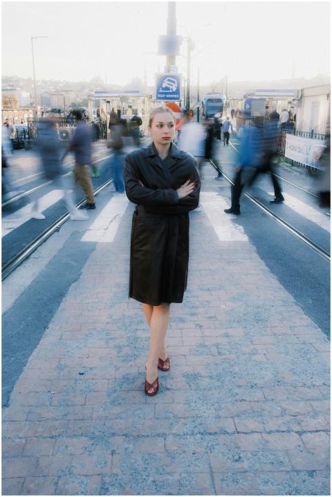 A woman in a coat stands still amidst a blurred cr