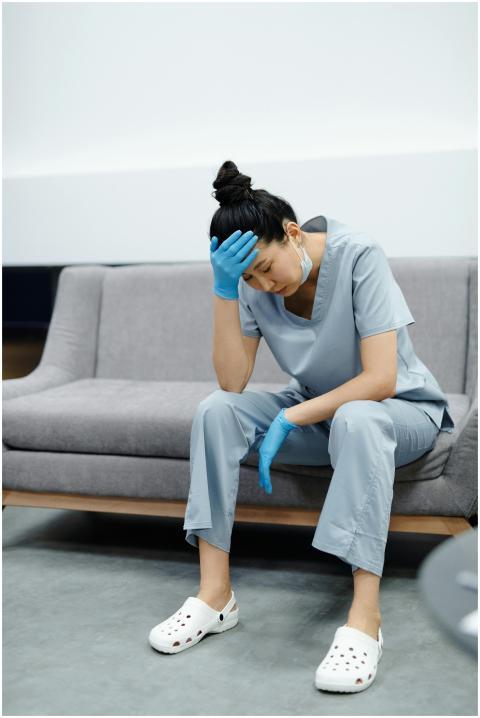 Tired nurse in scrubs sitting on a sofa, looking e