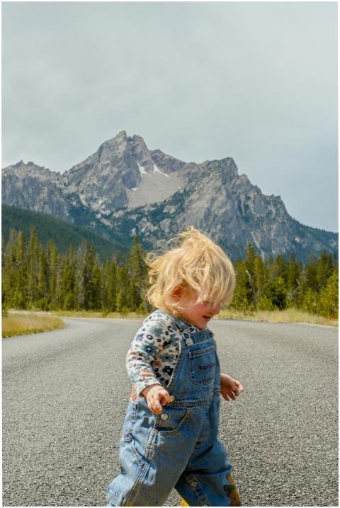 A young blonde child in denim overalls walks on a