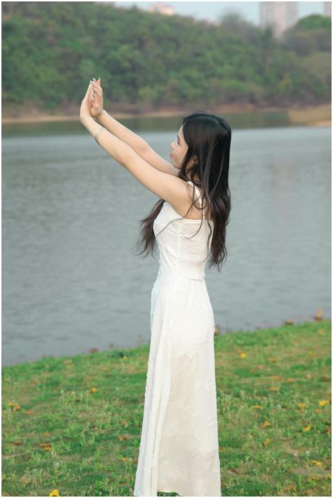 Elegant woman in white dress stands by a serene la