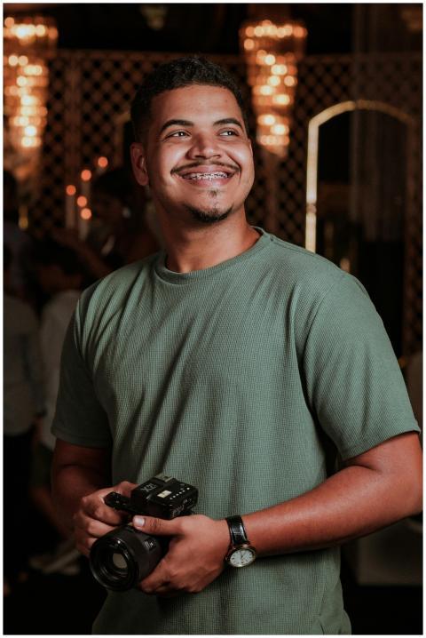 Smiling man with camera at indoor event, showcasin