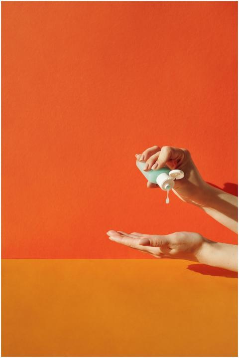 Hands applying sanitizer against vibrant orange ba