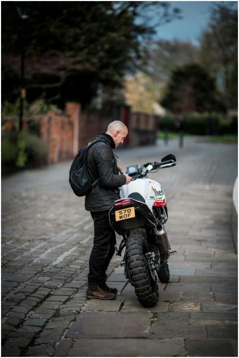 A man with a backpack stands beside a motorcycle o