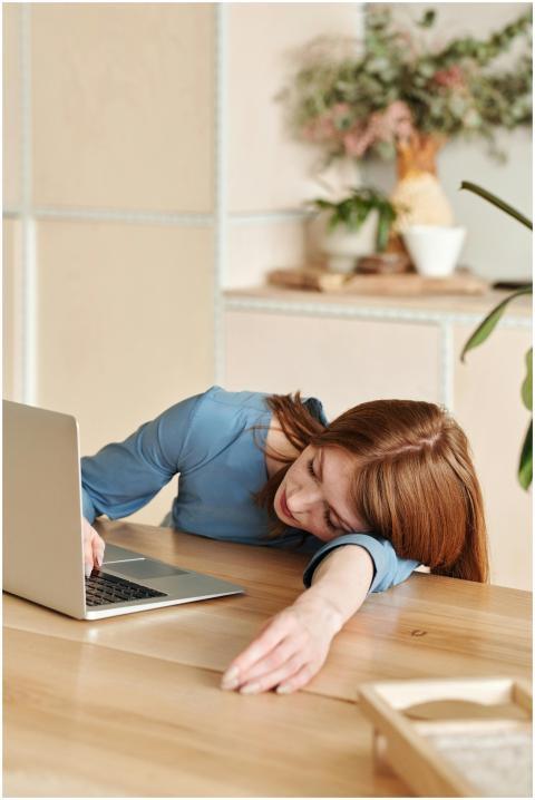 Woman in blue dress asleep on desk with laptop nea