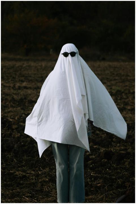 Person in a ghost costume wearing sunglasses stand
